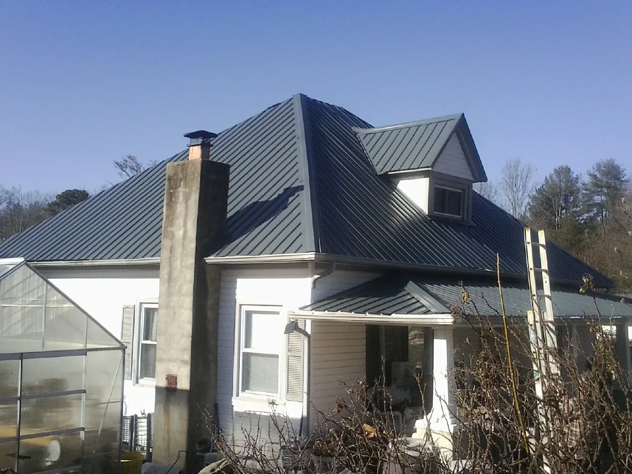 Dark blue standing seam metal roof on a white farmhouse with dormer — Slate & Tile Roof Repair by Roofing Brothers in Colbert