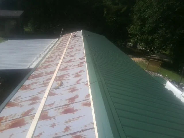 Old rusted panels beside newly installed green metal roofing — Wind Damage Roof Repair by Roofing Brothers in Colbert