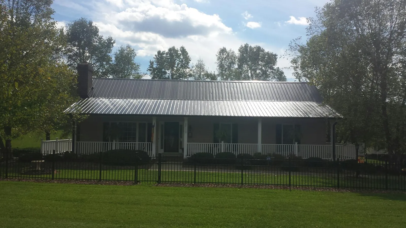 Gray metal roof on a brick ranch with a full width front porch — Gutter Guard Installation work by our crew in Colbert