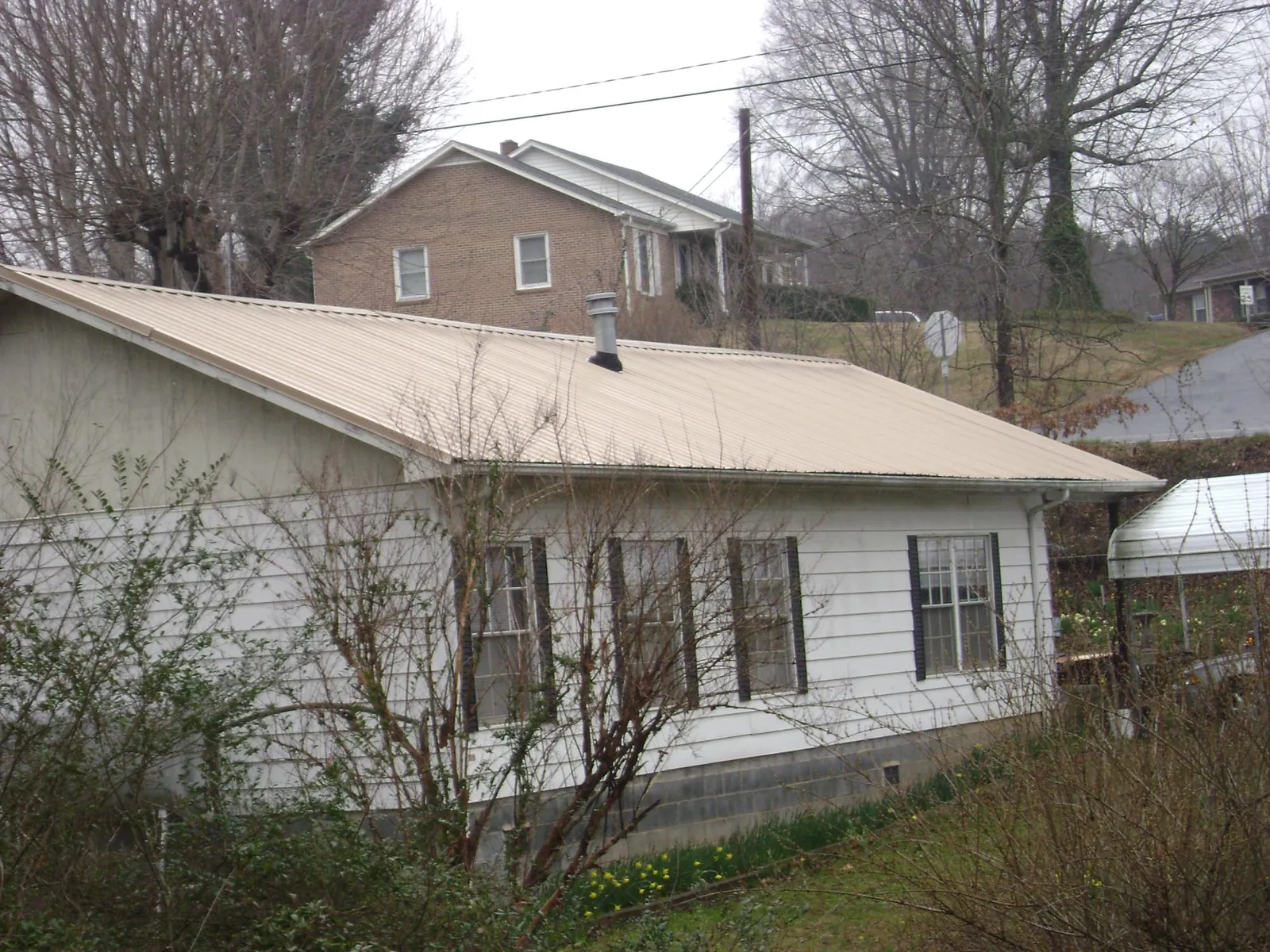 Tan metal roof on a white sided house set into a hillside — Commercial Roofing by Roofing Brothers in Colbert